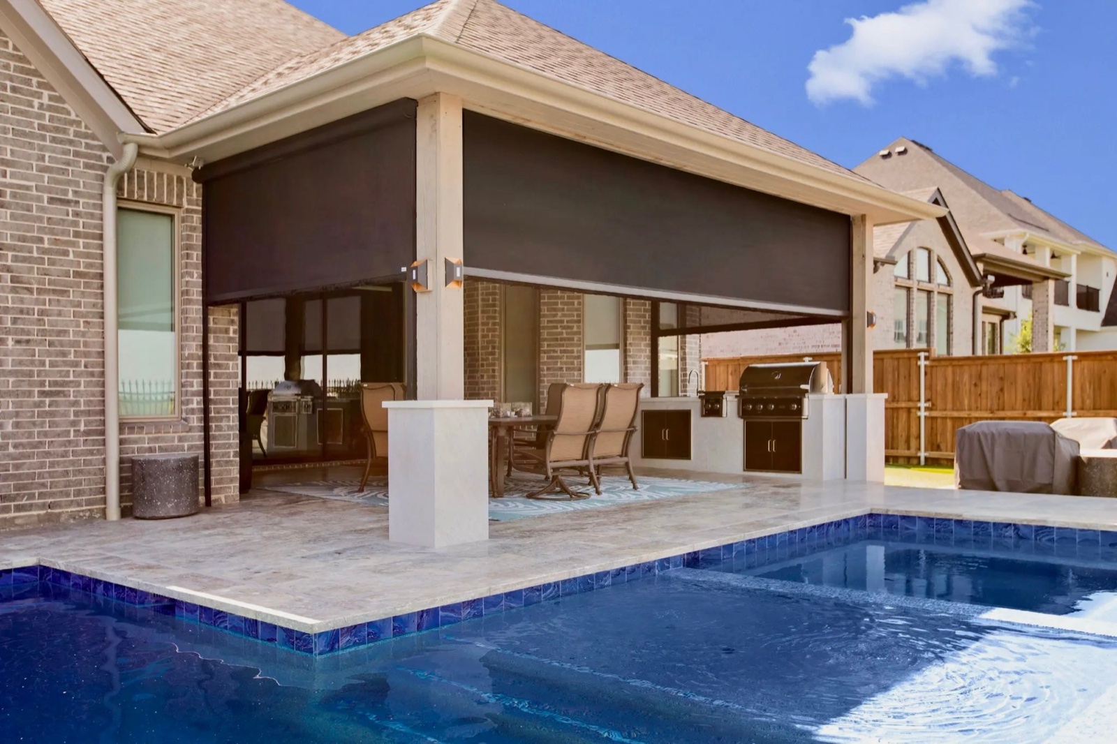 Motorized patio shades lowered over a covered patio beside a pool